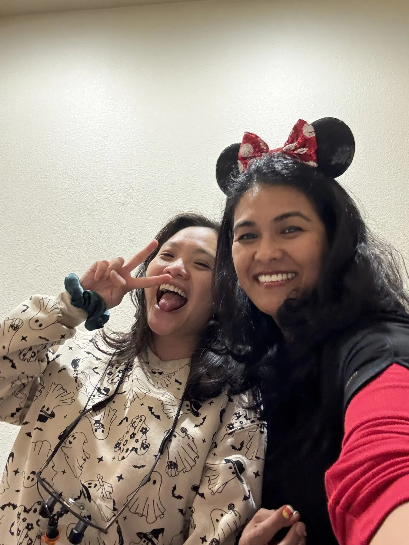 Two team members laughing in a selfie, one in a ghost-print sweater and one wearing Minnie Mouse ears