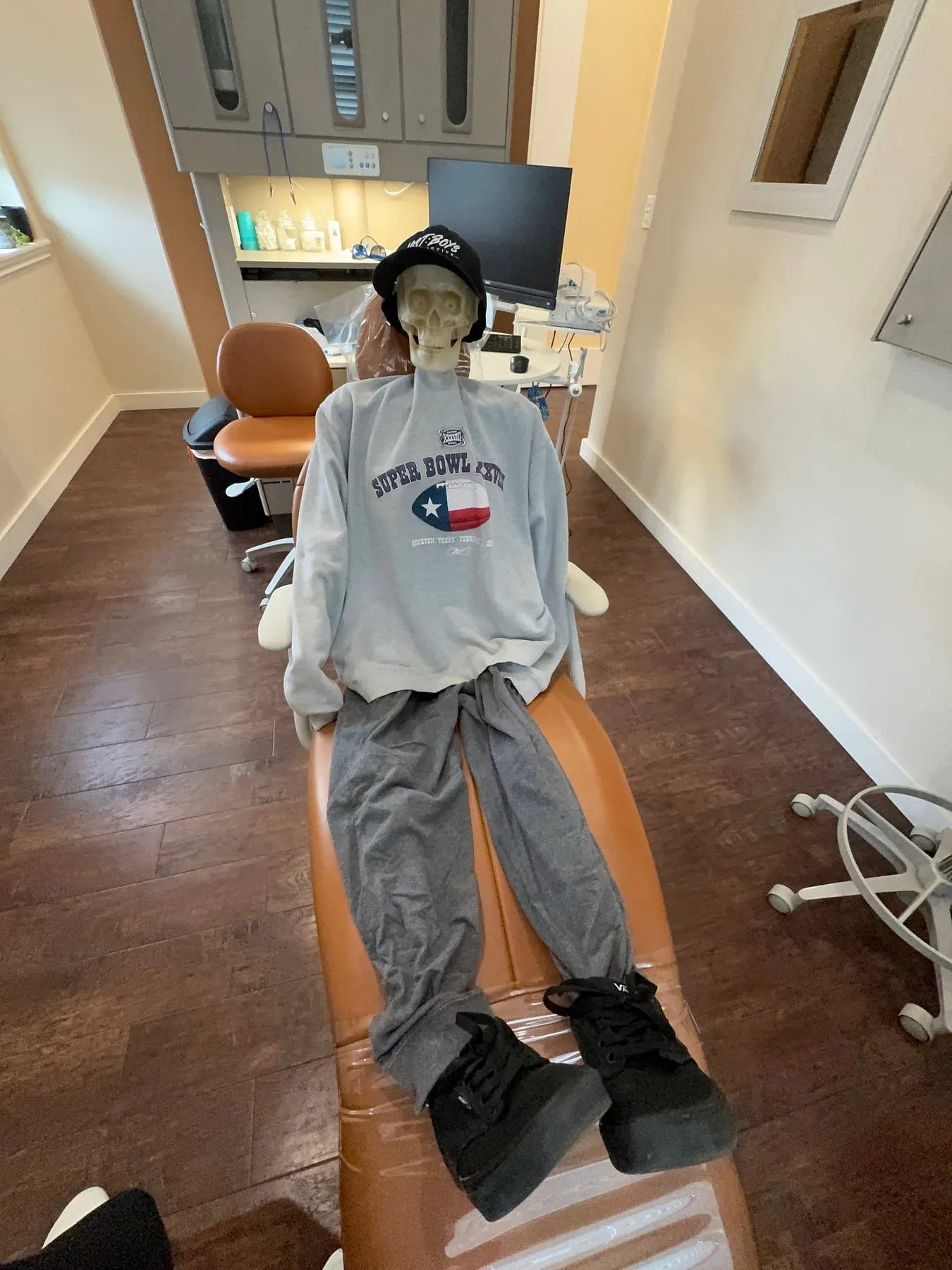 A skeleton in a Super Bowl sweatshirt, cap, and sneakers reclining in a dental chair at Hutto Hippo Family Dental