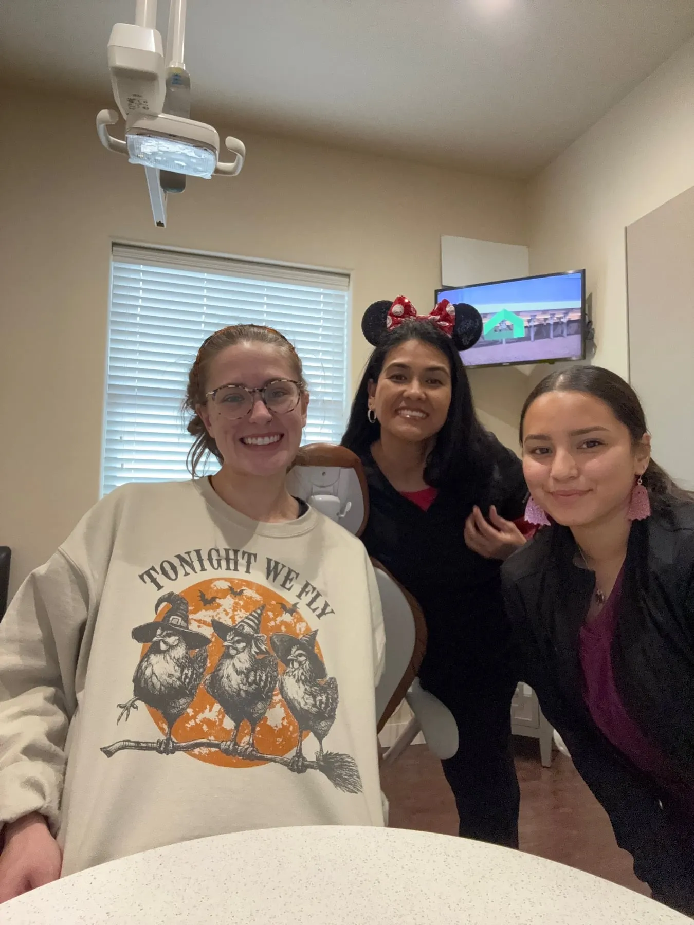 Three team members in a treatment room, one wearing a Tonight We Fly witch chicken sweatshirt
